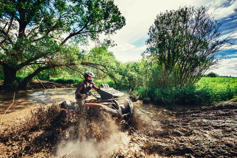 A rider in a helmet driving an ATV through a muddy stream