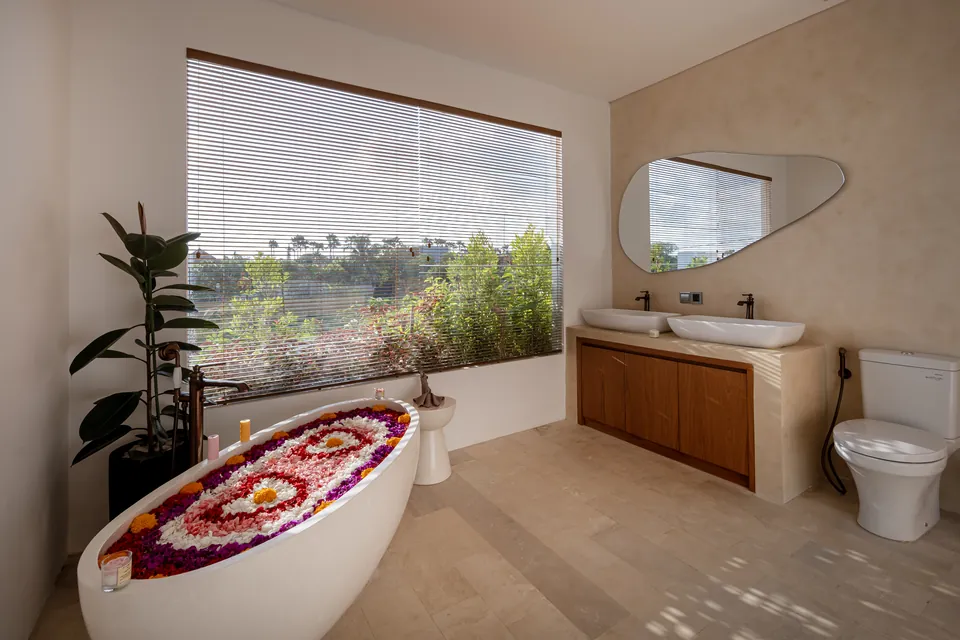 A flower-petal design in a freestanding bathtub beside a large window overlooking greenery
