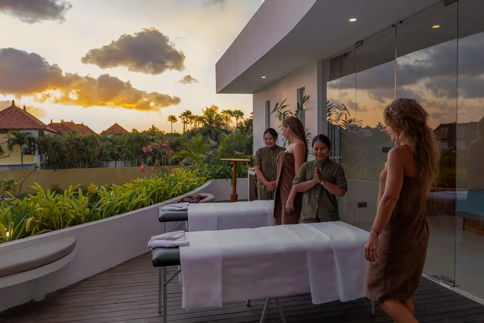 Two massage tables set on a villa terrace at sunset as the therapists welcome two guests in robes