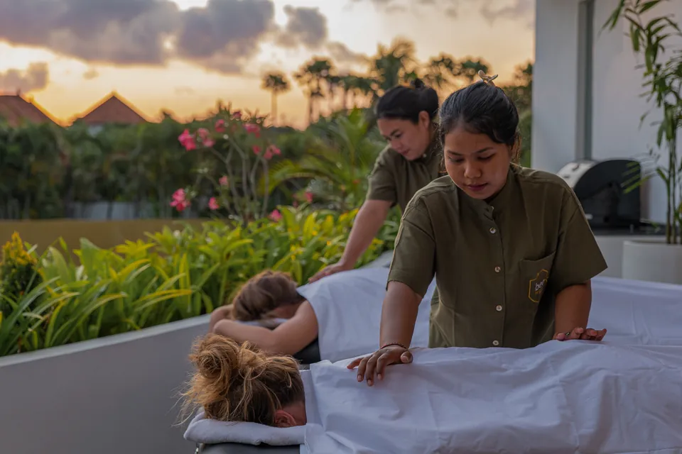 Two therapists giving massages to two guests on a villa terrace at sunset