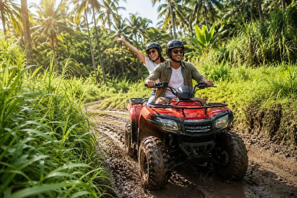 A rider and a waving passenger sharing a red ATV on a trail through palm trees