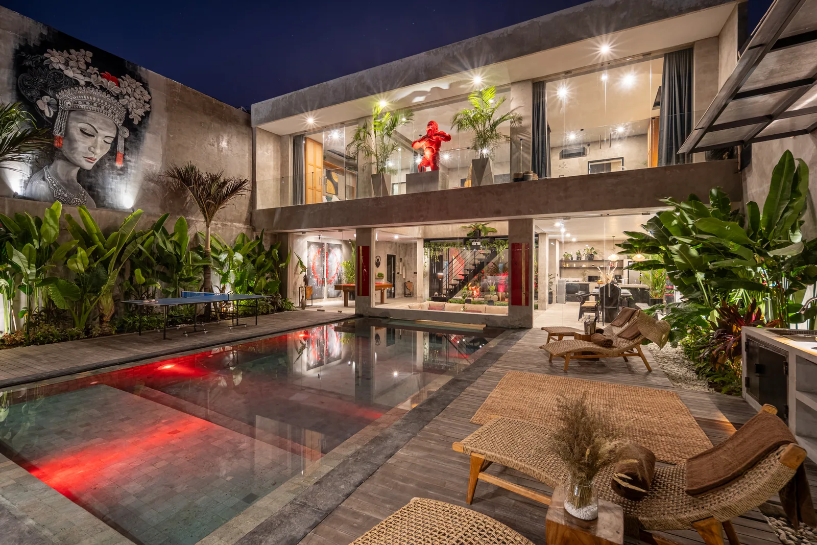 Concrete Serenity's pool courtyard at night, the bedrooms lit and a mural on the courtyard wall